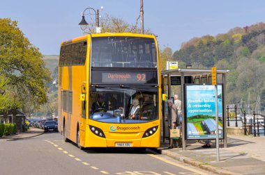 Dartmouth, Devon, İngiltere, İngiltere - 24 Nisan 2025: İnsanlar Dartmouth kasabasındaki bir otobüs durağında Posta Arabası servis otobüsüne biniyor.