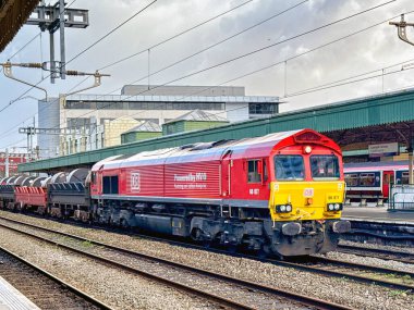 Cardiff, Wales, İngiltere - 24 Ekim 2025: 66. sınıf yük lokomotifi (66 077) Cardiff Merkez Demiryolu İstasyonu 'ndan ağır çelik bobinler taşıyan vagonları çekiyor