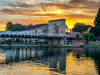 Marlow, Buckinghamshire, İngiltere - 20 Temmuz 2025: Marlow 'daki All Saints Kilisesi' nin manzaralı görüntüsü Thames Nehri 'nin yansımasıyla birlikte Marlow' daki zincir köprü.,