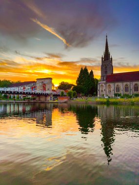 Marlow, Buckinghamshire, İngiltere - 20 Temmuz 2025: Marlow 'daki All Saints Kilisesi' nin manzaralı görüntüsü Thames Nehri 'nin yansımasıyla birlikte Marlow' daki zincir köprü.,