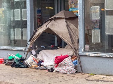 Bridgend, Wales, İngiltere - 14 Aralık 2025: Bridgend şehir merkezindeki kapalı bir dükkanın kapısında evsiz bir kabadayı çadır ve eşyaları.