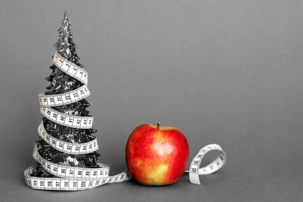 一根一厘米长的缎带包裹在一棵成熟苹果旁边的小玩具圣诞树上。圣诞假期健康食品的概念. — 图库照片