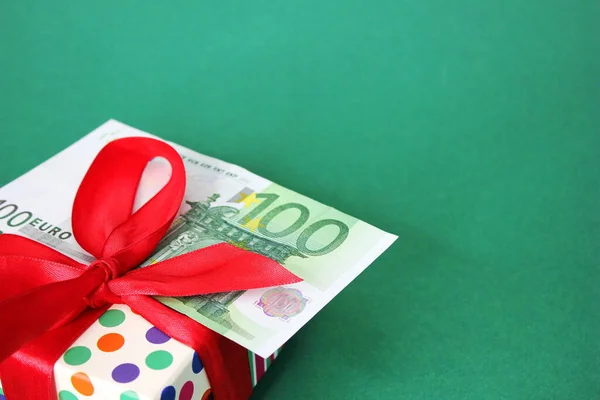 100 Euro banknote on a gift box with a red bow. Green background. — Stock Photo, Image