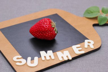 Tahta doğrama tahtasının üzerinde olgun kırmızı bir çilek. Tahta harflerle 