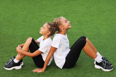 Aynı spor kıyafetleri içinde birbirine benzeyen iki kız kardeş stadyumun yeşil çimlerinde oturup birbirlerine bakıyorlar..