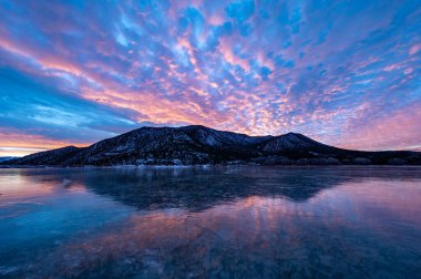 Renkli turuncu ve mavi günbatımı bulutları batı Colorado 'daki Harvey Gap Eyalet Parkı' ndaki donmuş göle yansıyor..
