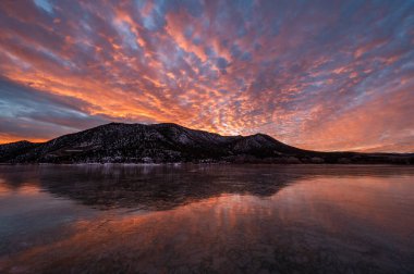 Renkli turuncu ve mavi günbatımı bulutları batı Colorado 'daki Harvey Gap Eyalet Parkı' ndaki donmuş göle yansıyor..