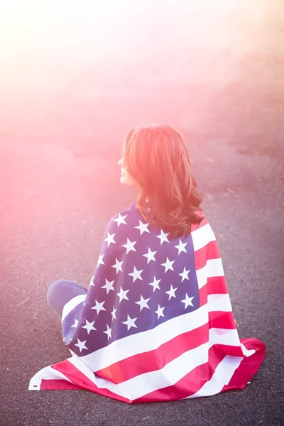 Dreaming patriot woman sitting down with american flag wrapped a — Stock Photo, Image