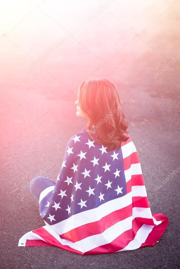 Dreaming patriot woman sitting down with american flag wrapped a