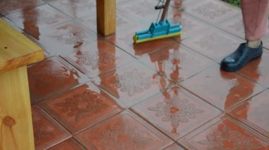 Kadın zemini suyla paspasla yıkıyor.