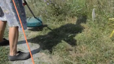 Kadın el budama makinesiyle çim biçiyor.