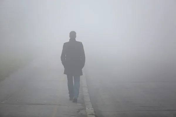 Homem com as costas andando pela rua de nevoeiro — Fotografia de Stock