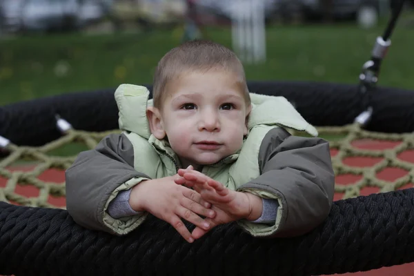 Niño pequeño en chaquetas de otoño balanceándose en un columpio — Foto de Stock