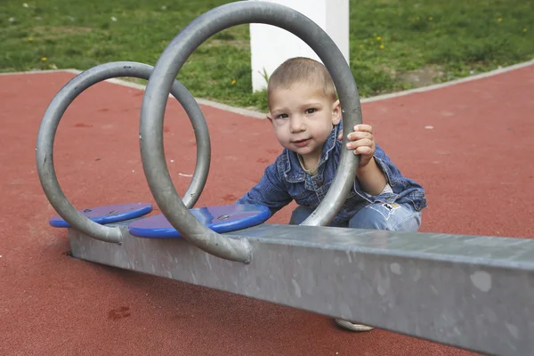 Niño feliz jugando al balanceo en el patio de recreo — Foto de Stock