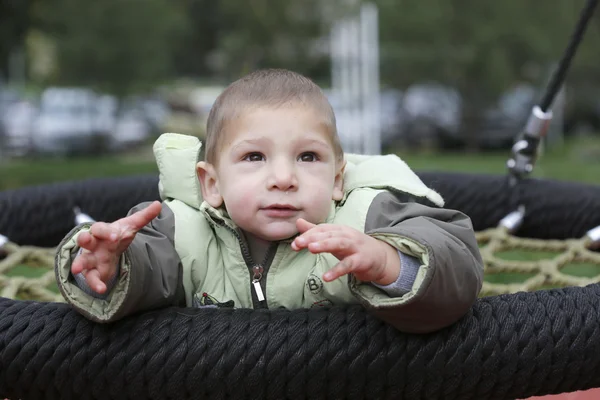 Niño pequeño en chaquetas de otoño balanceándose en un columpio — Foto de Stock