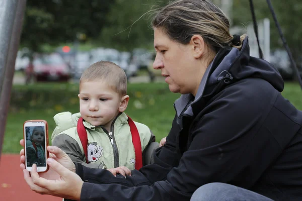 Mamá fotografiando selfie pequeño hijo con teléfono móvil en el parque — Foto de Stock