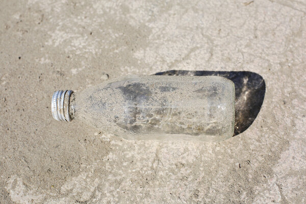 Отвергнутая старая бутылка в песке на асфальте
