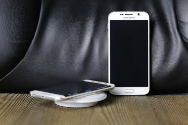 Ahşap masa üzerinde kablosuz şarj cihazı ile beyaz Samsung Galaxy S6 ve kenar atış