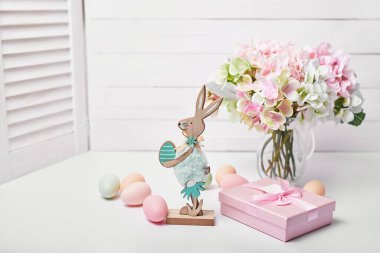 Mutlu Paskalya yumurtaları ve tavşan tebrik kartı. Çiçek buketi ve beyaz arka planda hediye kutusu
