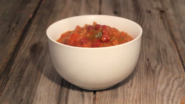 Pouring chili con carne in a bowl with cheese and onion topping closeup video — Stock Video