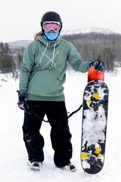 woman holding a snowdeck snowskate snowboard on top of the slope Bromont Quebec Canada