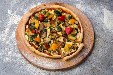 Biber, kabak, patlıcan, mozzarella peynirli vejetaryen pizza ahşap tabakta fesleğen pesto sosuyla servis edilir. Mutfak unuyla servis edilir..