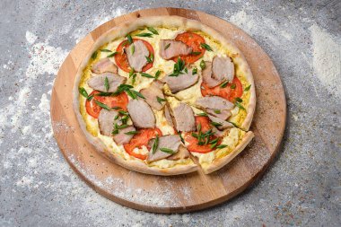 Et ve domates dilimli tam bir köy pizzası. Taze taze taze soğan soğan soğanı, ahşap tabakta taze un ve gri beton arka planda baharatla servis ediliyor..