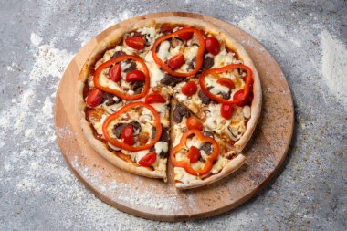 Ahşap tabakta tam etli pizza. Mutfak unu ve gri beton arka planda baharatlar servis ediliyor. Biftek parçalı fast food yemeği, kiraz domatesleri, kırmızı biber (tatlı dolma biber) ve mozzarella peyniri. 
