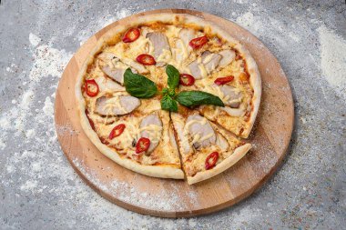 Baharatlı pizza dilimlenmiş domuz eti ve tavuk eti, mozzarella peyniri, acılı biber dilimleri ahşap tabakta taze fesleğenle servis edilir mutfak unu ve beton arka planda baharatlar ile servis edilir.