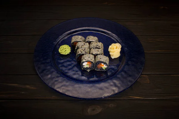 顶部的日本寿司卷与生姜和芥末放在深蓝色的玻璃板上 木制背景 奶油芝士 用黑米包裹的飞鱼 — 图库照片