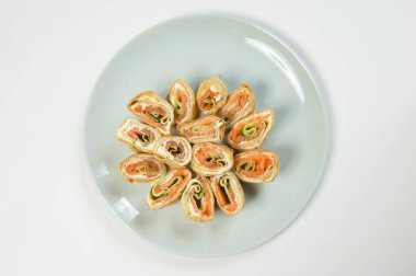 Philadelphia krem peyniri, somon balığı ve salatalık dilimli Rus başlangıç tabağı blini. Krepe sarılmış marine edilmiş kırmızı balık filetosu. Taze sebzeli deniz ürünleri.