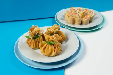 Geleneksel Rus kreplerinin yan görünüşü. Et ve somon balıklı Blini. Noel tatili yemekleri. Yeni yıl servisi. Mavi soyut arka planda servis edilen ince Rus krepleri.