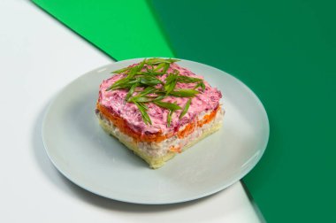 Geleneksel Rus Shuba salatasının yanında sebze katmanları ve balık filetosu. Tüylü pancar salatasının altında ringa. Renkli yeşil arka planda taze soğan soğanı ile servis ediliyor.