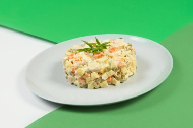 Geleneksel Rus Noel Olivier salatası. Mayonez soslu haşlanmış sebze tabağı. Yılbaşı soğuk tabağı yeşil renkli soyut arka planda gri tabakta servis edilir