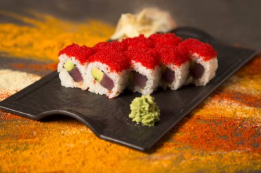 Japon deniz mahsullü suşi dürümünü ton balığı Maguro ve avokado ile kapatın. Kırmızı uçan balık yumurtası Tobiko, wasabi ve zencefil ile servis edilir. arkaplana saçılmış zerdeçal, sarımsak, köri, paprika baharatları