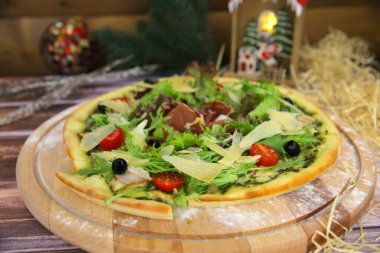 Yakın plan İtalyan pizzası ahşap tabakta servis edilir ve arka planda yılbaşı süsü vardır. Fast food, taze marul, jambon, jambon, jambon, parmesan peyniri, zeytin, domates.
