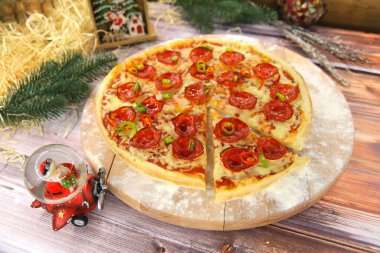 İtalyan pepperonili pizza ahşap tabakta servis ediliyor ve yeni yıl süsleri arka planda. Salamlı fast food yemeği, kırmızı ve yeşil biber dilimleri ve mozzarella peyniri.