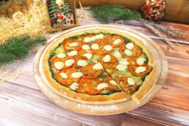 Caprese salatasında İtalyan pizzasının yan görüntüsü ahşap tabakta servis edilir ve arka planda yeni yıl süsü vardır. Fesleğen soslu vejetaryen yemeği, domates dilimleri ve mozzarella peyniri.