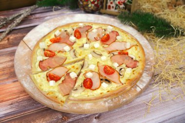 Ahşap tabakta servis edilen lezzetli İtalyan etli pizzası ve arka planda Noel süsü. Füme tavuk ve pastırma dilimli fast food yemeği, feta peyniri, şampiyon mantarlar, vişneli domates.