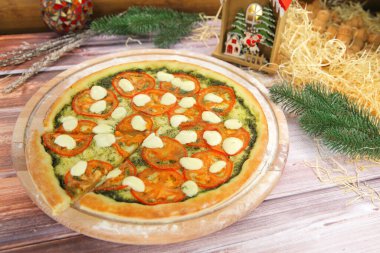Caprese sebze salatasında İtalyan pizzası ahşap tabakta servis edilir ve arka planda yılbaşı süsü vardır. Fesleğen soslu vegan yemeği, domates dilimleri ve mozzarella peyniri.