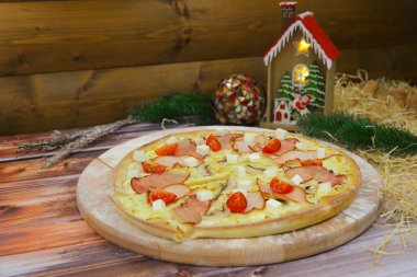 Tahta tabakta servis edilen İtalyan etli pizzasının yan görünüşü ve arka planda Noel süsü. Füme tavuk ve pastırma dilimli fast food yemeği, feta peyniri, şampiyon mantarlar, vişneli domates.