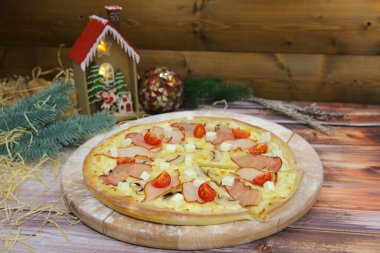 Ahşap tabakta servis edilen İtalyan etli pizzasının yakın plan resmi ve arka planda Noel süsü var. Füme tavuk ve pastırma dilimli fast food yemeği, feta peyniri, şampiyon mantarlar, vişneli domates.