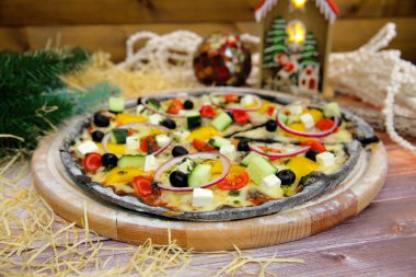 İtalyan siyah hamurlu vejetaryen pizzasını ahşap tabakta ve masada servis et ve arka planda yeni yıl süsü olsun. Fast food sebze yemeği taze salatalık, domates, paprika, feta