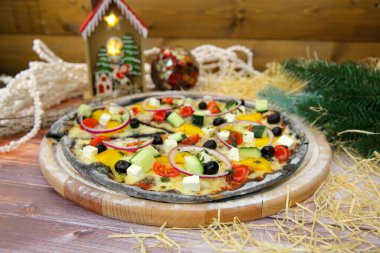 İtalyan siyah hamurlu vejetaryen pizzası ahşap tabakta ve masada servis ediliyor ve arka planda yeni yıl süsü var. Fast food sebze yemeği taze salatalık, domates, paprika, peynir.