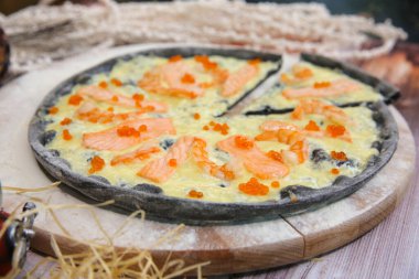 Tahta tabakta servis edilen İtalyan siyah hamurlu pizza makrosu ve arka planda yılbaşı süslemeleri. Somon dilimleri, kara kaplan karidesleri ve kırmızı havyarlı fast food deniz ürünleri.