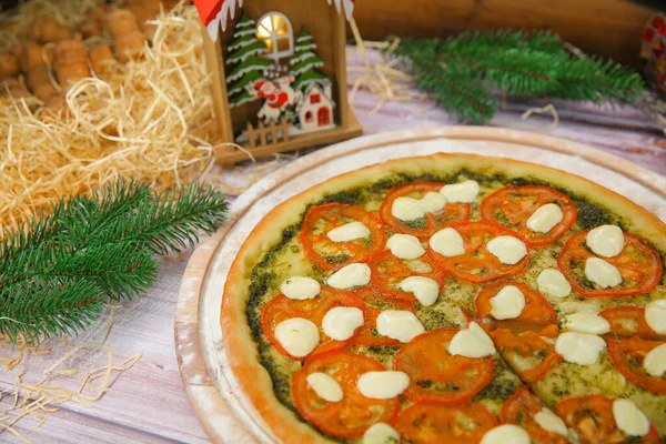 Close up of Italian vegetablepizza in Caprese salad style served on wooden plate with Christmas new year decoration on background. veggie dish with pesto sauce, tomato slices and mozzarella cheese