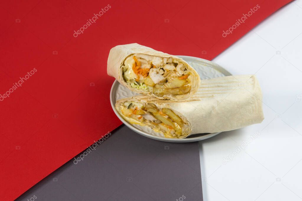 Chicken meat cheesy Shawarma roll with cabbage, carrot, French fries, cheese wrapped in lavash bread served on red, brown and white abstract background. Gyros Street food grilled doner