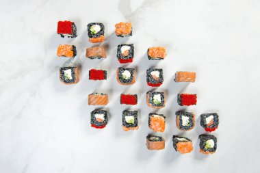 Beyaz mermer arka planda servis edilen siyah pirinç suşi rulolarının hemen üstünde. Somon, avokado, krem peynir ve kırmızı uçan balık yumurtası Tobiko (Masago) ile suşi. Büyük deniz ürünleri suşisi seti.