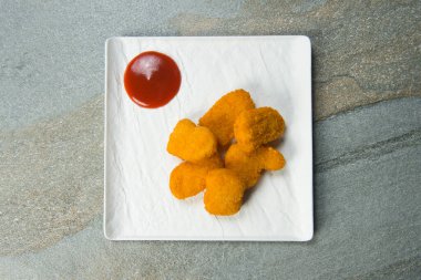 Beyaz kare tabakta kırmızı domates ve ketçap sosuyla servis edilen altı tavuk parçasının tam üstünde. Gri antrasit taşından arka plan. Minimalist yemek menüsü konsepti. Boşluk resmini kopyala