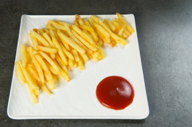 Kırmızı ketçap soslu patates kızartması. Beyaz tabakta, koyu taştan arka planda. Minimalist tarzda servis edilen fast food menüsünü yemeye hazır.. 